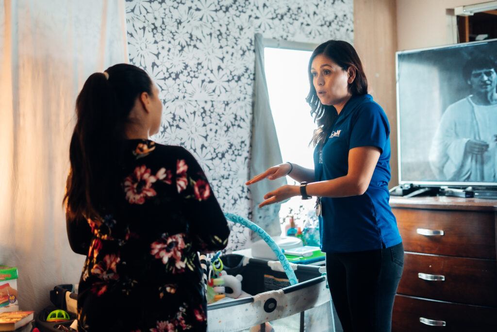 Two women talking near a baby crib.