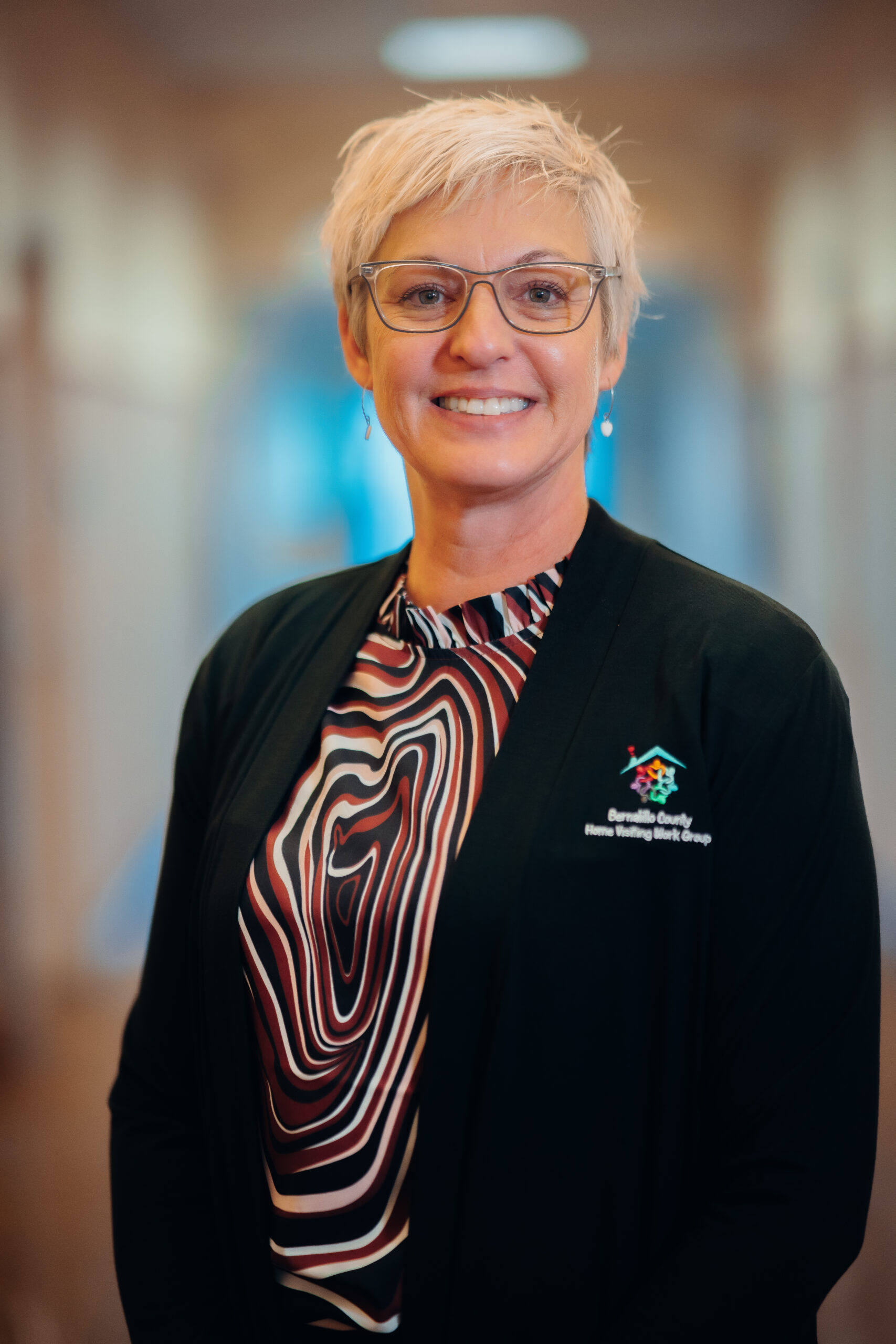 Smiling woman in black blazer with logo.